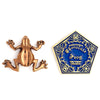 Pin dorado con diseño de rana de chocolate de Harry Potter junto a tarjeta Honeydukes